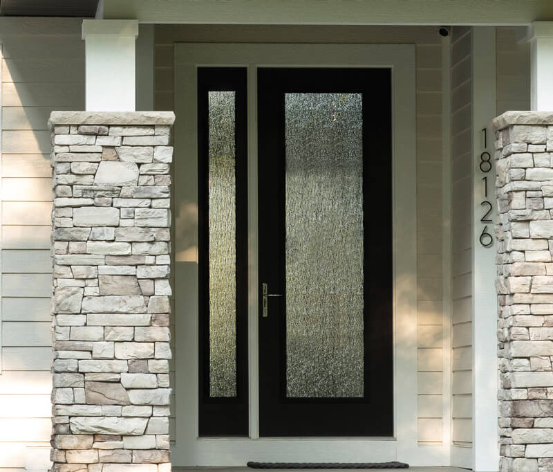 A modern entry door with frosted glass panels and a sleek black frame is flanked by stone columns. The house number 18126 is displayed vertically on the right, complementing the light-colored siding.