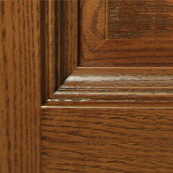 Close-up of a fiberglass panel with a rich brown finish, showcasing natural grain patterns and a beveled edge, complementing the sleek design of a fiberglass door. The polished wood features distinct horizontal and vertical lines marking the panels design.