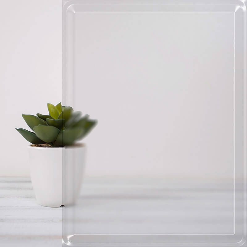 A small green succulent plant in a white pot sits on a light wooden surface. Half of the image is covered by a transparent, glossy sheet, reminiscent of window glass with reflective coating, slightly distorting the view of the plant. The background is a soft white.