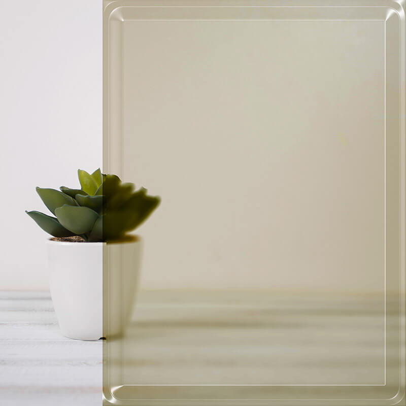 A small green succulent in a white pot sits on a light wooden surface. A sheet of tinted glass, often used for windows, partially covers the plant, creating a subtle split effect in the background.